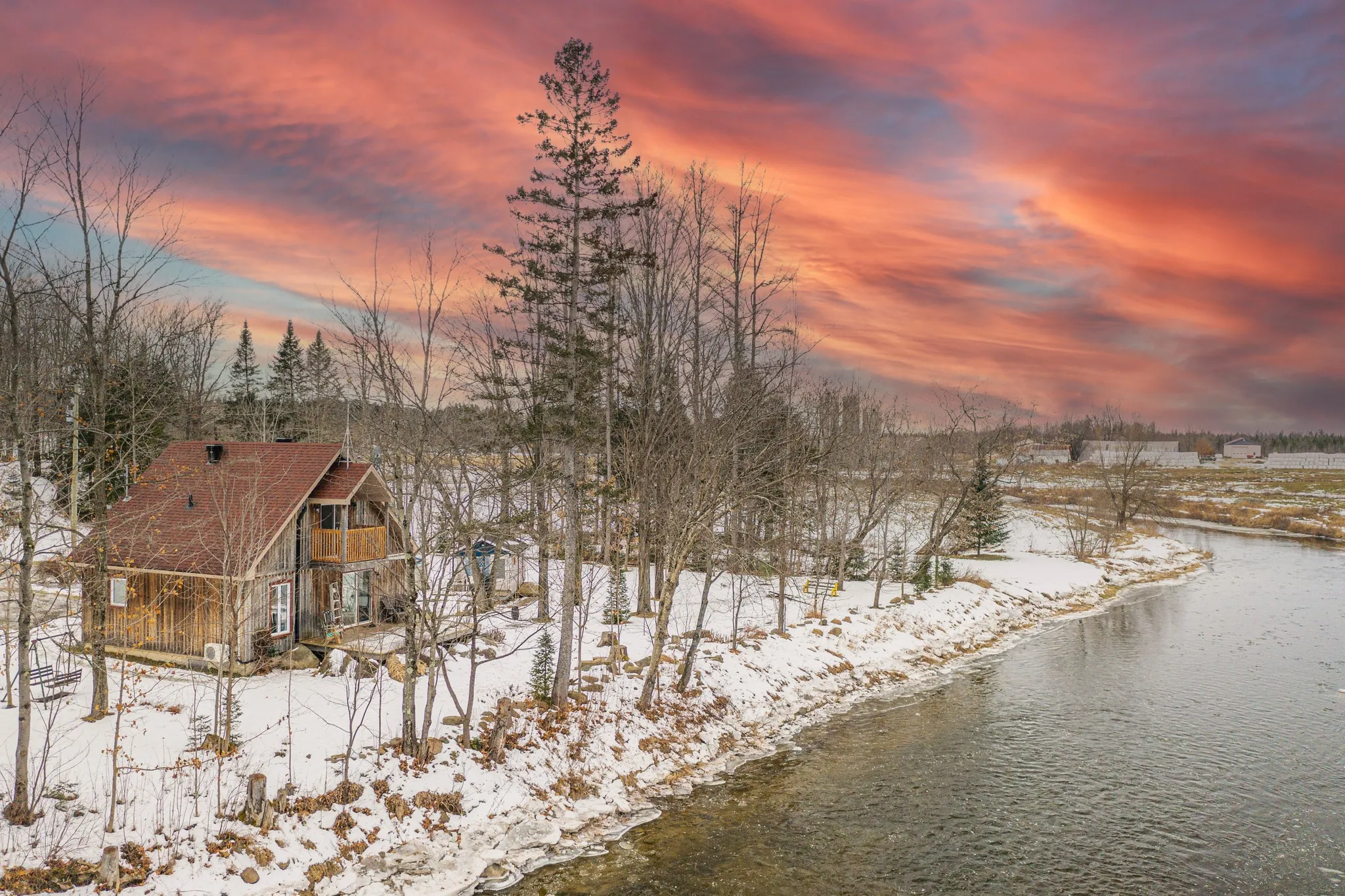 Chalet au bord de la rivière sous ciel coloré.